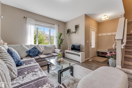 Bright living area featuring large windows, wood-finish flooring, a built-in entry bench, and carpeted stairs - 1514 26 Avenue Nw, Edmonton, AB - Indoor Photo Showing Living Room