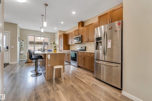 Open-concept kitchen featuring wood-finish flooring, stainless steel appliances, a center island with pendant lighting, wood cabinetry, and a subway tile backsplash - 1514 26 Avenue Nw, Edmonton, AB - Indoor Photo Showing Kitchen With Upgraded Kitchen