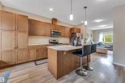 Contemporary kitchen featuring wood-finish cabinetry, stainless steel appliances, a subway tile backsplash, and a central island with pendant lighting - 