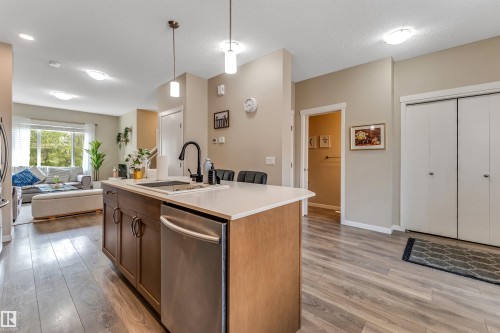Kitchen island with a white countertop and integrated sink, stainless steel dishwasher, wood-finish flooring, and recessed lighting - 1514 26 Avenue Nw, Edmonton, AB - Indoor Photo Showing Kitchen