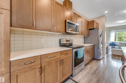 Modern kitchen featuring wood-finish cabinetry, stainless steel appliances, light-toned countertops, a subway tile backsplash, and wood-finish flooring - 1514 26 Avenue Nw, Edmonton, AB - Indoor Photo Showing Kitchen