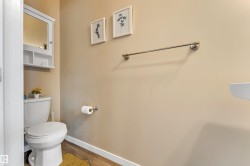 Bathroom featuring wood-finish flooring, a white toilet, and a wall-mounted white medicine cabinet with mirrored door - 