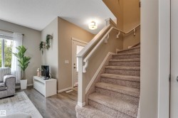 Carpeted staircase with white railings, wood-finish flooring, and a window with white sheer curtains - 