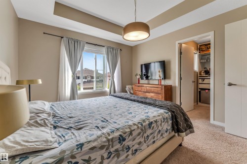 Carpeted room featuring a large window, tray ceiling, and a built-in closet with shelving and drawers - 1514 26 Avenue Nw, Edmonton, AB - Indoor Photo Showing Bedroom