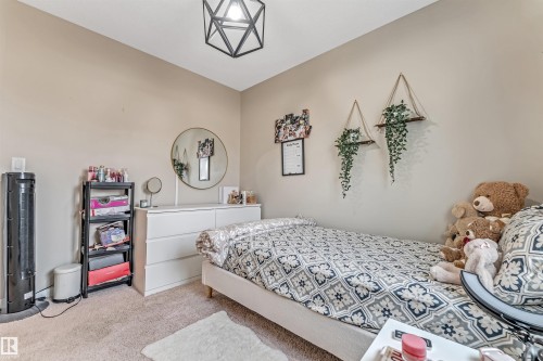 Carpeted room featuring a white dresser, a wall-mounted round mirror, and a geometric semi-flush mount light fixture - 1514 26 Avenue Nw, Edmonton, AB - Indoor Photo Showing Bedroom