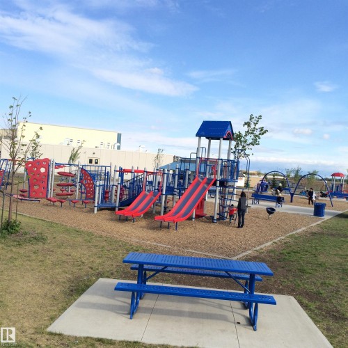 Expansive recreational area featuring multiple play structures, a picnic table on a concrete pad, and a wood chip surface - 1839 80 Street Sw, Edmonton, AB 