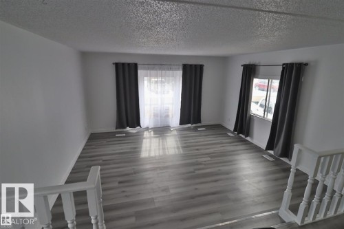 Bright living space featuring wood-finish flooring, white walls, and multiple windows - 98 Willow Park Estates, Leduc, AB 