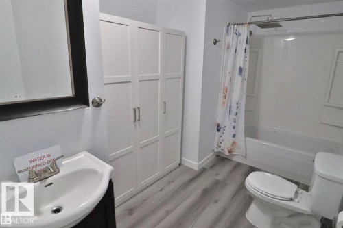 Vanity with basin sink, framed mirror, built-in storage cabinetry, wood-finish flooring, and a shower-tub combination - 98 Willow Park Estates, Leduc, AB 