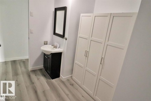 Wood-finish flooring, white walls, dark wood-tone vanity, wall-mounted mirror, and white storage cabinets - 98 Willow Park Estates, Leduc, AB 