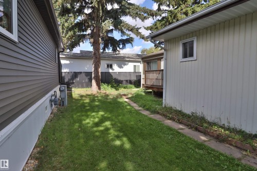 Side yard featuring a grassy area, concrete stepping stones, and mature trees - 98 Willow Park Estates, Leduc, AB 