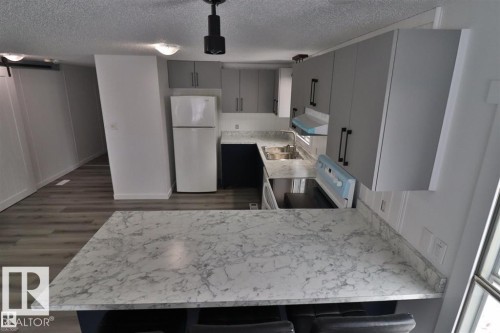 Kitchen featuring a breakfast bar with stone-look countertop, wood-finish flooring, grey cabinetry, and white appliances - 98 Willow Park Estates, Leduc, AB 
