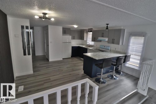 Open-concept kitchen featuring two-tone cabinetry, a central island with an extended countertop, and wood-finish flooring - 98 Willow Park Estates, Leduc, AB 