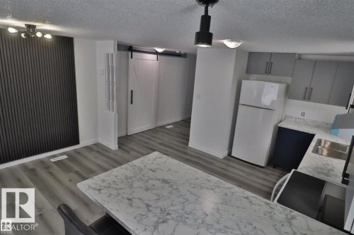 Wood-finish flooring throughout, paired with a white barn door and a dark vertical slat accent wall - 98 Willow Park Estates, Leduc, AB 