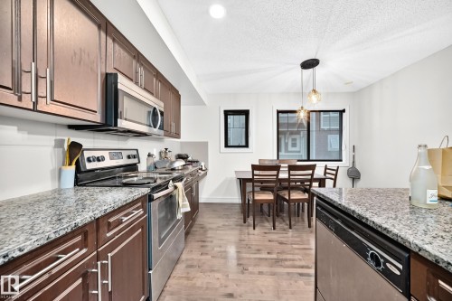 Kitchen featuring stainless steel appliances, dark wood cabinetry, and speckled countertops - #146 655 Tamarack Rd Nw, Edmonton, AB 
