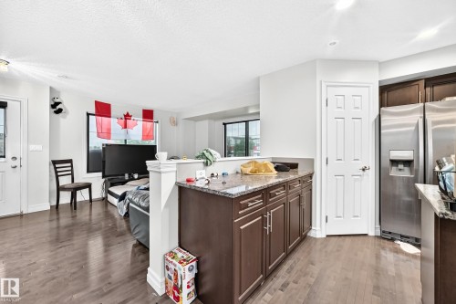 Wood-finish flooring throughout, kitchen with dark wood cabinetry, and stainless steel French door refrigerator - #146 655 Tamarack Rd Nw, Edmonton, AB 
