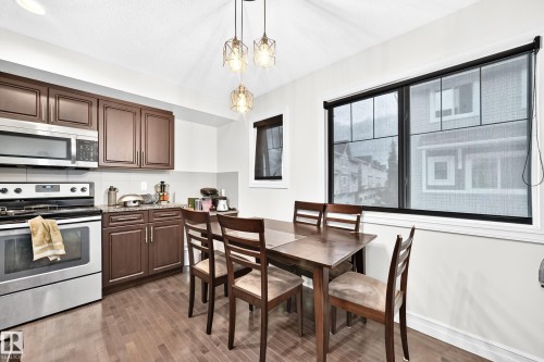 Compact kitchen featuring wood-finish flooring, stainless steel appliances, dark wood cabinetry, and a light-toned backsplash - #146 655 Tamarack Rd Nw, Edmonton, AB 