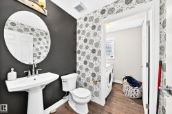 Pedestal sink with a circular mirror, wall-mounted light fixture, and patterned accent wall - 