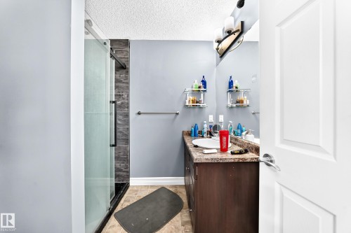 Shower with sliding glass enclosure, wood-finish vanity with an integrated sink, broad wall mirror, and overhead light fixture - #146 655 Tamarack Rd Nw, Edmonton, AB 