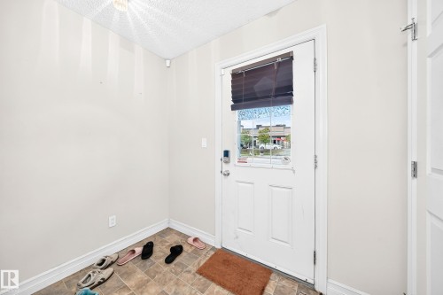 White paneled door with glass insert, textured ceiling, and tile flooring - #146 655 Tamarack Rd Nw, Edmonton, AB 