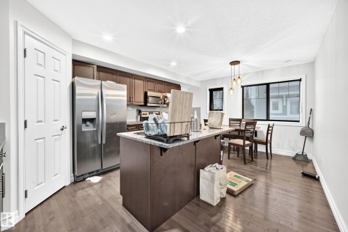 Kitchen featuring wood-finish flooring, stainless steel appliances, dark wood cabinetry, a granite-top island, and recessed lighting - #146 655 Tamarack Rd Nw, Edmonton, AB 