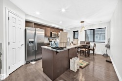 Kitchen featuring wood-finish flooring, stainless steel appliances, dark wood cabinetry, a granite-top island, and recessed lighting - 