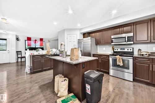 Kitchen featuring wood-finish flooring, dark wood cabinetry, a center island with a speckled countertop, and stainless steel appliances - #146 655 Tamarack Rd Nw, Edmonton, AB 