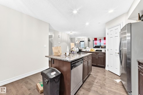 Kitchen island with dark wood-finish cabinetry, integrated dishwasher, and a speckled countertop - #146 655 Tamarack Rd Nw, Edmonton, AB 