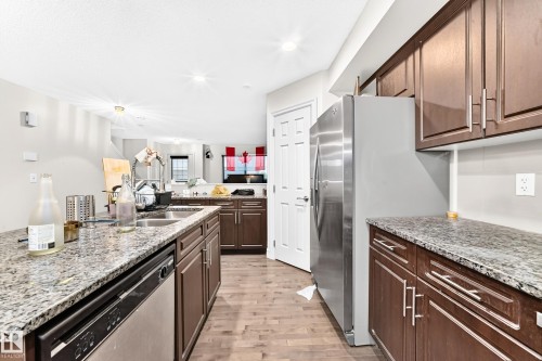 Kitchen with wood-finish flooring, stainless steel appliances, granite countertops, and wood cabinetry - #146 655 Tamarack Rd Nw, Edmonton, AB 