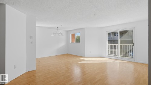 Spacious interior with light wood-finish flooring, white walls, and a contemporary chandelier - #107 10153 117 St Nw, Edmonton, AB 