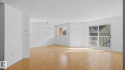 Spacious interior with light wood-finish flooring, white walls, and a contemporary chandelier - 