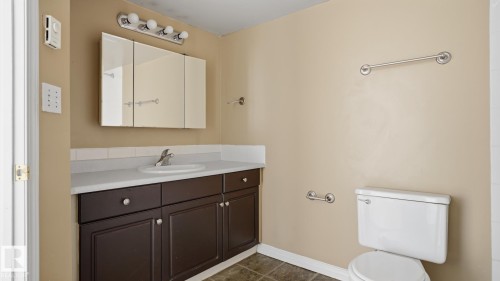 Bathroom featuring a dark wood finish vanity with integrated sink, white countertop, and a triple-door mirrored medicine cabinet - #107 10153 117 St Nw, Edmonton, AB 