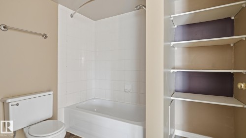 White bathtub with tiled surround, white toilet, and built-in shelving unit - #107 10153 117 St Nw, Edmonton, AB 