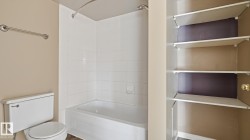 White bathtub with tiled surround, white toilet, and built-in shelving unit - 