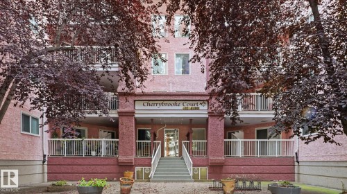Cherrybrooke Court building entrance featuring a prominent sign, white railings, and a multi-level facade - #107 10153 117 St Nw, Edmonton, AB 