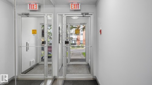 Double glass doors with aluminum frames, illuminated "EXIT" signs, and grey floor mats - #107 10153 117 St Nw, Edmonton, AB 