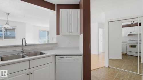 Kitchen featuring a double stainless steel sink, white dishwasher, white cabinetry, and tiled flooring - #107 10153 117 St Nw, Edmonton, AB 