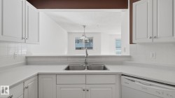 White cabinetry with silver hardware, dual basin stainless steel sink with a high-arc faucet, tiled backsplash, and white countertops - 
