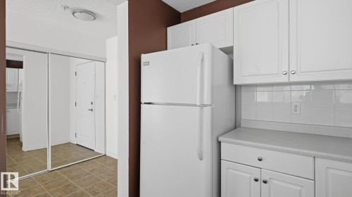 White paneled cabinetry, light-colored countertops, white tile backsplash, and ceramic tile flooring - #107 10153 117 St Nw, Edmonton, AB 