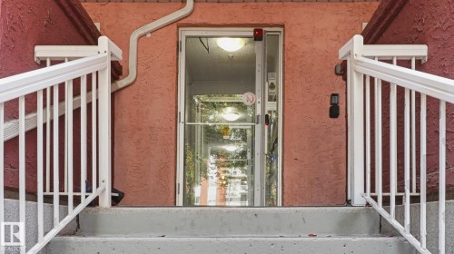 Concrete steps with white railings lead to a glass-paneled entrance door - #107 10153 117 St Nw, Edmonton, AB 