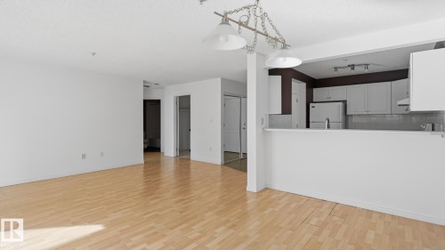 Hardwood-style flooring throughout, an open kitchen concept, white cabinetry, integrated refrigerator, and a tile backsplash - #107 10153 117 St Nw, Edmonton, AB 