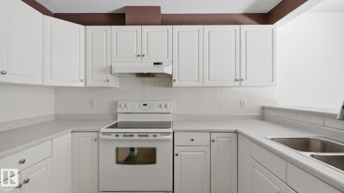 White shaker-style cabinetry, white appliance suite, dual basin stainless steel sink, tiled backsplash, and light-toned countertops - #107 10153 117 St Nw, Edmonton, AB 