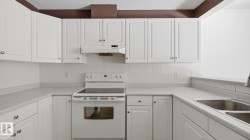 White shaker-style cabinetry, white appliance suite, dual basin stainless steel sink, tiled backsplash, and light-toned countertops - 