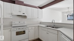White cabinetry with silver-tone hardware, white tile backsplash, stainless steel double basin sink, and white appliances - 