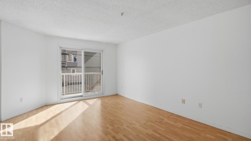 Sliding glass door, light wood-finish flooring, white walls, and a private balcony with white railings - #107 10153 117 St Nw, Edmonton, AB 