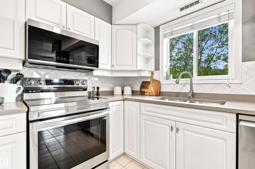 White cabinetry with stainless steel appliances, solid surface countertops, and a tile backsplash - #432 6703 172 St Nw, Edmonton, AB 
