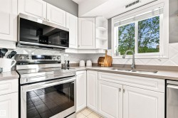 White cabinetry with stainless steel appliances, solid surface countertops, and a tile backsplash - 