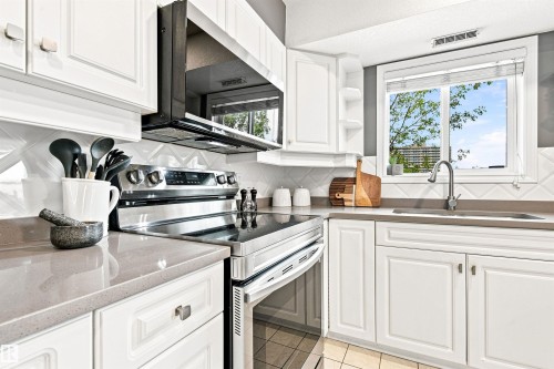 White shaker-style cabinetry, stainless steel appliances, light gray countertops, white geometric tile backsplash, and a stainless steel sink - #432 6703 172 St Nw, Edmonton, AB 