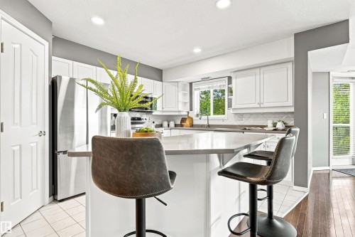 Kitchen featuring a central island with countertop seating, white shaker-style cabinetry, stainless steel appliances, and a tiled backsplash - #432 6703 172 St Nw, Edmonton, AB 