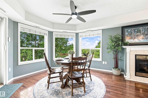 Bay window with multiple panes, ceiling fan light fixture, wood-finish flooring, fireplace with tile surround, and a white mantelpiece - #432 6703 172 St Nw, Edmonton, AB 