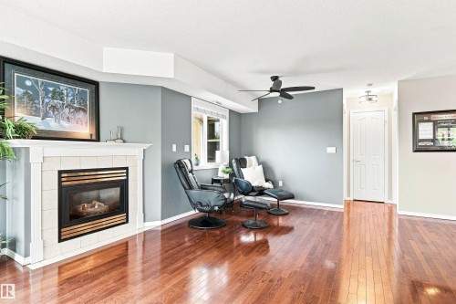 Hardwood-finish flooring, a fireplace with a tile surround and mantel, a ceiling fan, and a paneled door - #432 6703 172 St Nw, Edmonton, AB 